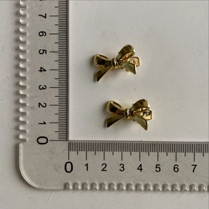 Detailed view of two mini gold metal bow hair clips with 2.5cm ruler scale measurements