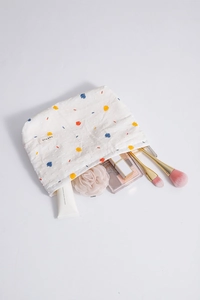 Detail shot of white cotton makeup bag with colorful embroidery and beauty products inside