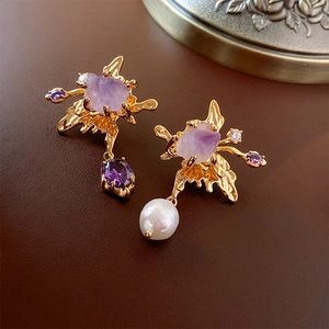 Macro detail of asymmetric gold earrings with purple amethyst and baroque pearls