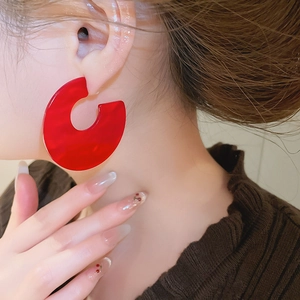 Close-up of model wearing bright red acrylic C-shaped earrings with a glossy finish