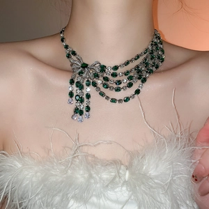 Detail of zircon bow necklace featuring emerald green gems and cascading tassel fringe