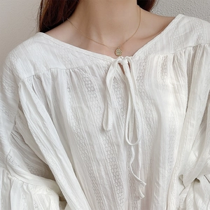 Close-up of golden textured circular pendant necklace worn with a white chic blouse