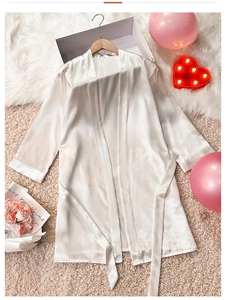 Detail of white satin bathrobe with waist tie and smooth silk-like texture on fur rug