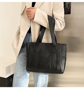 Detail of a large black leather tote bag worn by a model in a beige blazer and jeans