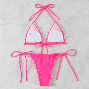Detail of neon pink bikini with white scalloped trim and lace-up ties on marble background