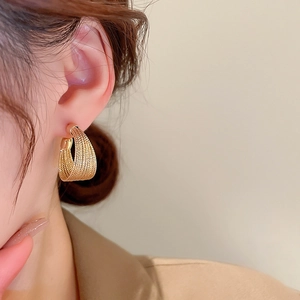Detail of warm gold geometric loop earring worn on ear against clean beige background
