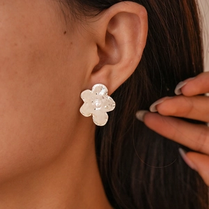 Close-up of minimalist silver flower stud earring with a white pearl on model's ear
