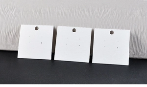 Macro shot of three white square jewelry display cards with hanging holes on a textured surface
