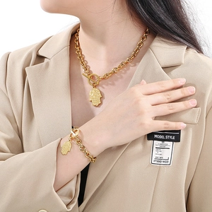 Goldenes Hamsa-Hand Anhänger-Halsketten und Armband-Set auf beigeem Blazer getragen