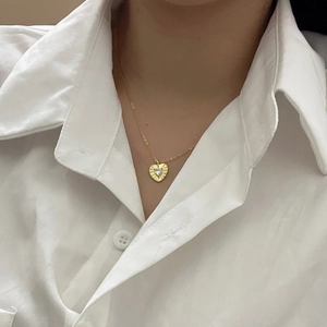 Detailed view of a gold heart pendant with radial texture on a delicate chain necklace