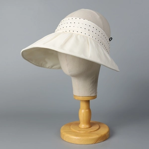 Beige organza open-top sun hat with black polka dot ribbon on a display stand