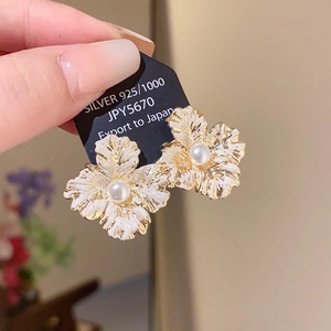 Detail of floral earrings with white enamel petals and a centered pearl on 925 silver needles