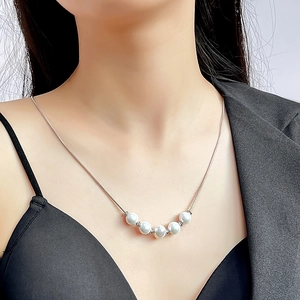 Close-up of five white pearls on a silver snake chain necklace worn by a model