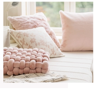 Close-up of a pink hand-woven thick yarn cushion and pillows in a cozy setting