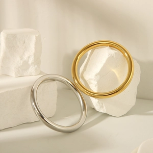 Polished gold and silver minimalist bangles resting on textured white stone decor