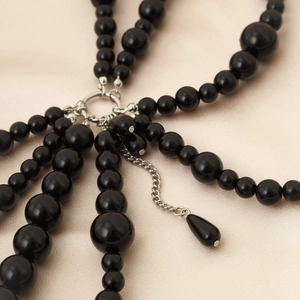 Close-up of multilayer black faux pearl body chain with silver teardrop pendant