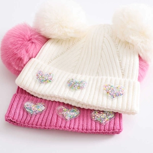 Detail of baby knit beanies in pink and white with pom-poms and sequin heart patches