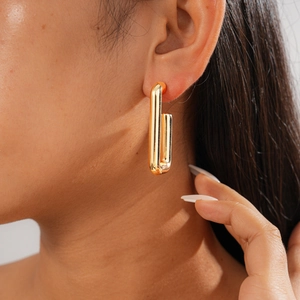 Close-up of minimalist rectangular gold earrings with metallic gloss on a model's ear