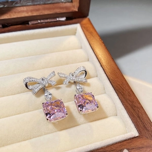 Macro shot of silver bow earrings with pink gemstone in a wooden jewelry box