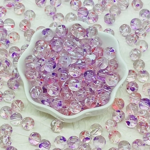 Close-up of translucent round glass beads with purple and red floral patterns in a white bowl