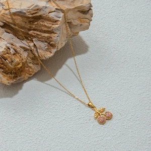 Macro shot of gold cherry necklace with pink crystals on a natural stone surface
