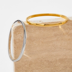 Brazaletes ovalados minimalistas de acero inoxidable en oro y plata sobre bloque de piedra