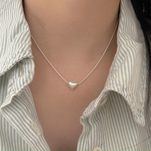 Close-up of minimalist sterling silver heart pendant necklace on a striped shirt