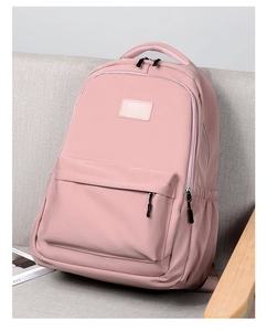 Pink nylon backpack with front zipper pocket shown on a gray fabric sofa