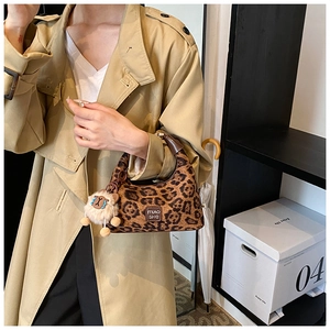 Close-up of leopard print baguette bag with plush sheep charm and brown leather handle