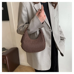 Detail view of a brown crocodile pattern crescent handbag held by a model in a gray blazer