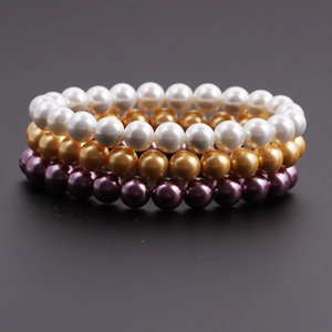 Vue détaillée de trois bracelets de perles en blanc, doré et violet sur fond sombre