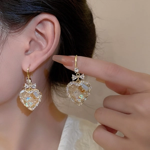 Close-up of golden bow and heart earrings with ice-crushed zircon crystals on model