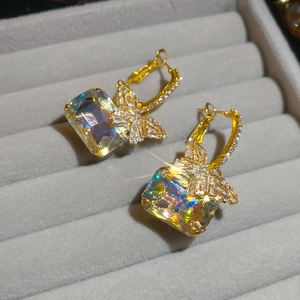 Macro detail of gold butterfly earrings with a square-cut sparkling zircon on velvet