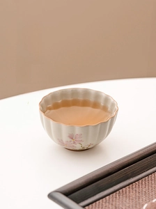 Close-up of ceramic tea cup with pink daisy motifs on scalloped edge with tea