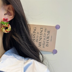 Close-up of a beaded Christmas wreath earring with a red bow on model's ear