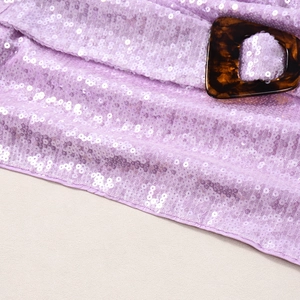 Dettaglio di paillettes viola e fibbia tartarugata su un completo gonna sexy da donna