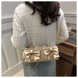Détail de vue arrière d'un sac cylindrique beige orné de grands nœuds décoratifs