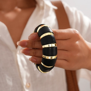 Detail of chunky acrylic elastic bracelet with matte black and gold metal links on a model
