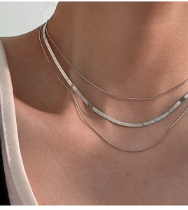 Detailed close-up of a three-layered silver snake chain necklace on a model neckline