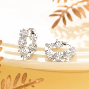 Silver star-shaped zircon hoop earrings displayed on a cream tray with golden leaves