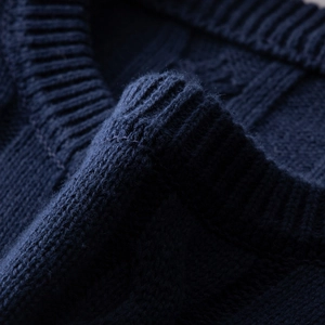 Close-up of dark blue cable knit sweater showing rib crew neck and textured shoulder detail