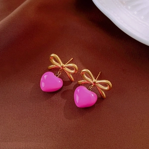 Détail des boucles d'oreilles nœud doré avec des pendentifs en forme de cœur rose poli