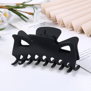 Close-up of matte black geometric hair claw clip with floral and fan props background