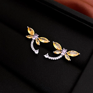 Close-up of a silver dragonfly earring with yellow, purple, and white stones on black velvet