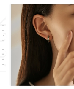 Detail shot of a silver hoop earring featuring a vibrant green heart pendant on a model
