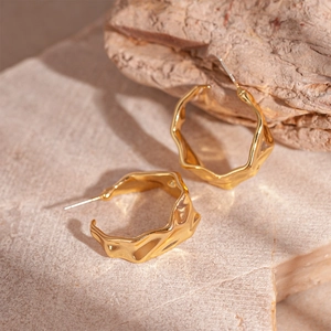Macro detail of gold C-shape earrings with molten metal texture on stone background