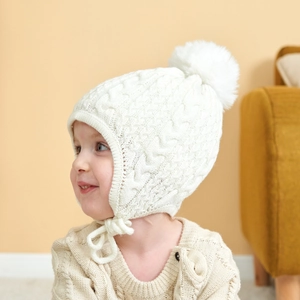 Close-up of cable knit baby hat with soft white pom-pom and protective earflaps