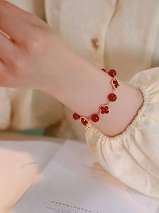 Close-up of red agate four-leaf clover charm and beaded bracelet with gold accents