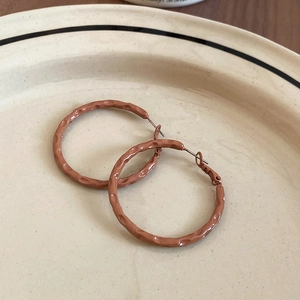 Detail of retro terracotta hoop earrings with hammered texture on a beige ceramic plate
