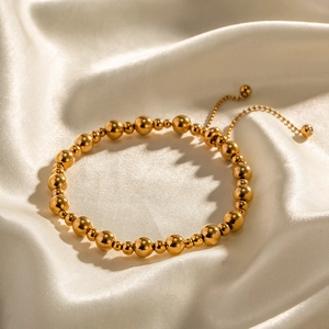 Verstellbares 18K vergoldetes Edelstahl-Perlenarmband auf cremefarbenem Seidenstoff